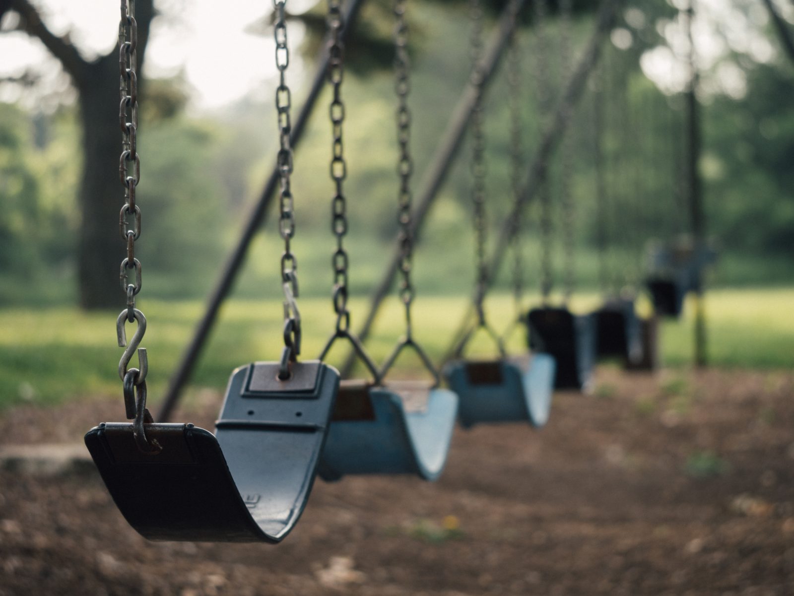 A row of empty swings on a playground swingset
